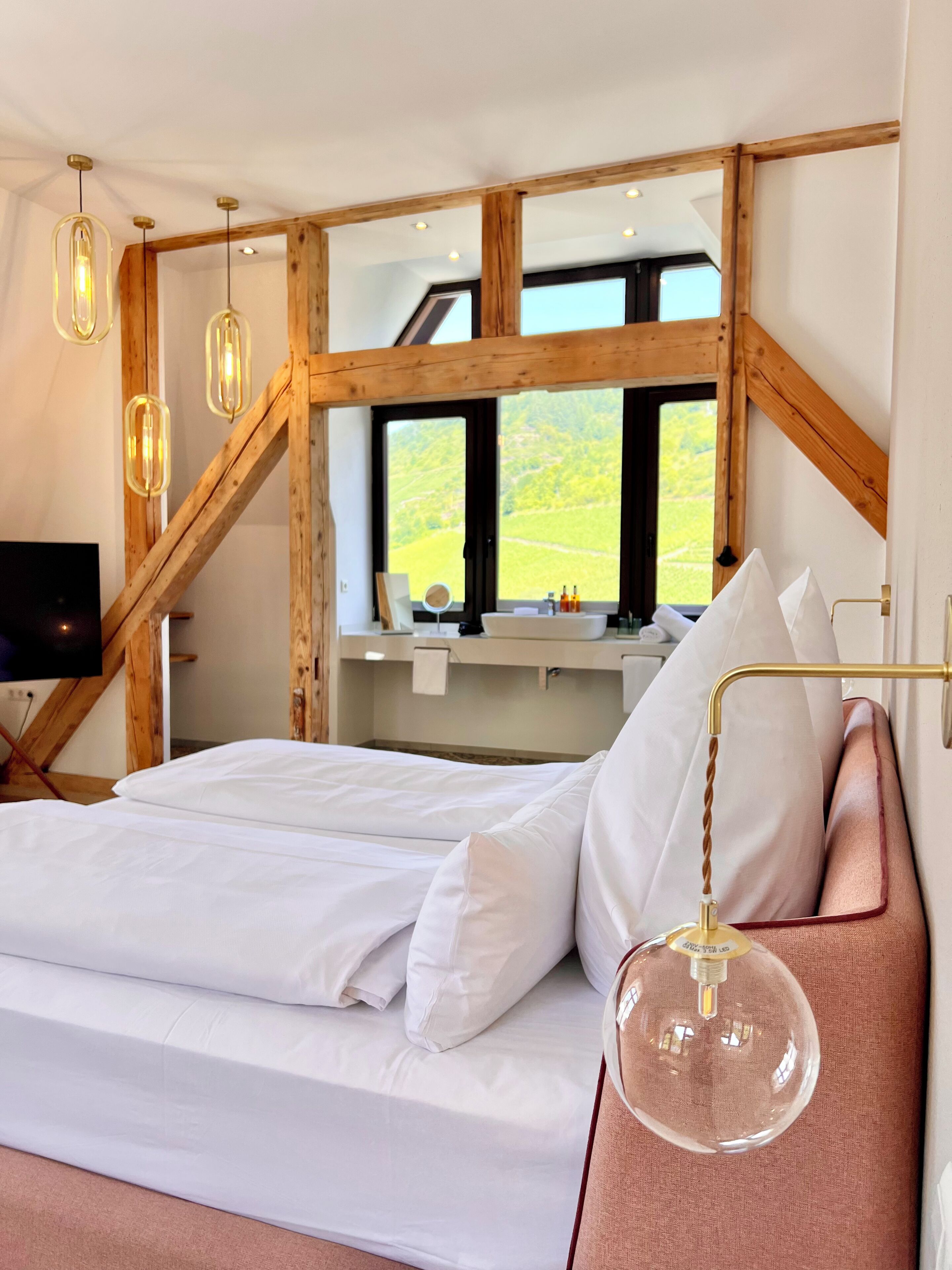 Une chambre avec un grand lit, des poutres apparentes, une télévision et une vue sur la verdure.