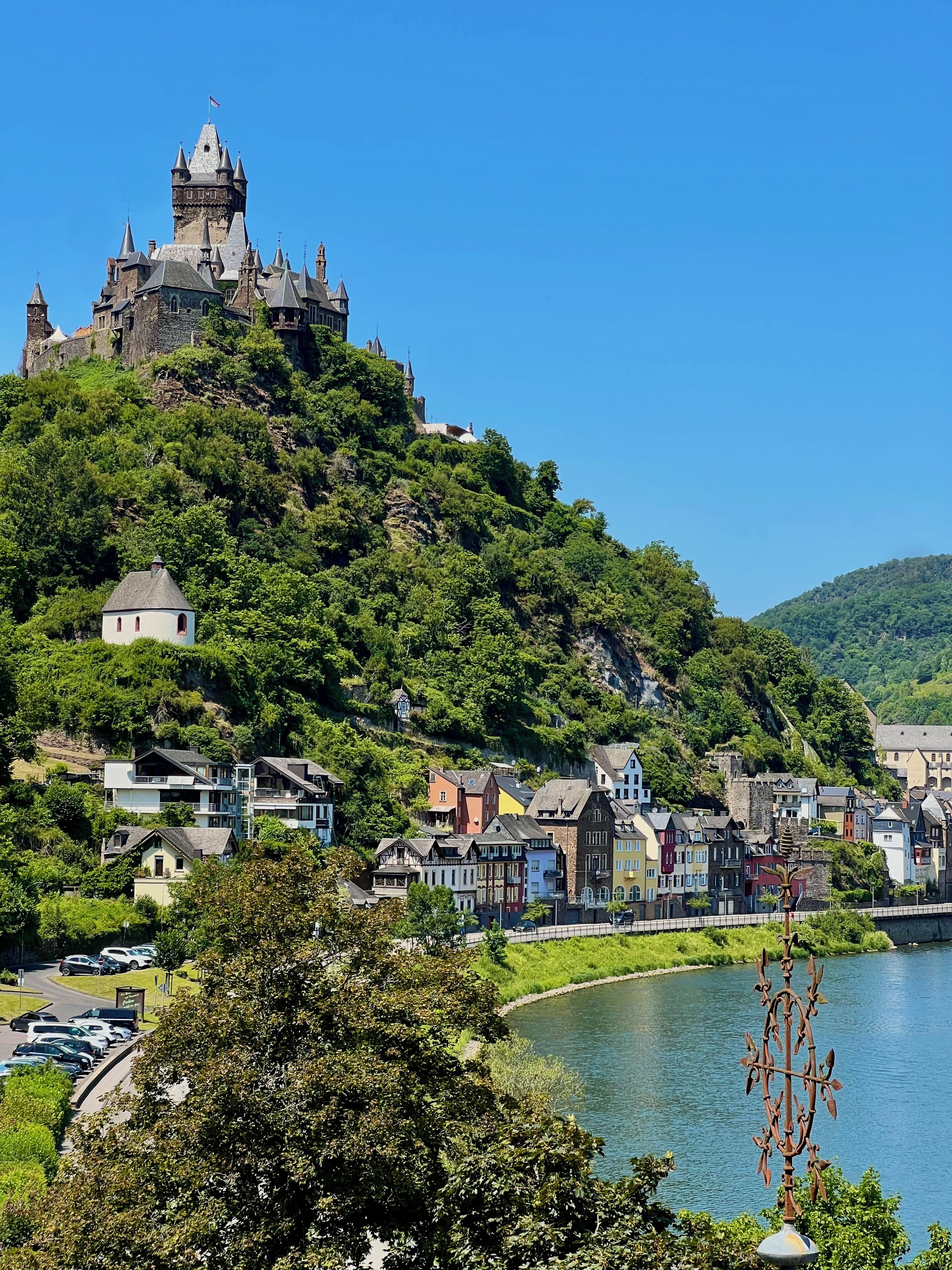 Eine Burg auf einem Hügel, darunter eine Stadt, ein Fluss und parkende Autos.
