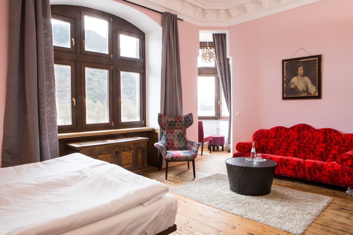 A room with a bed, a red sofa, a chair, a table, and a window with curtains.