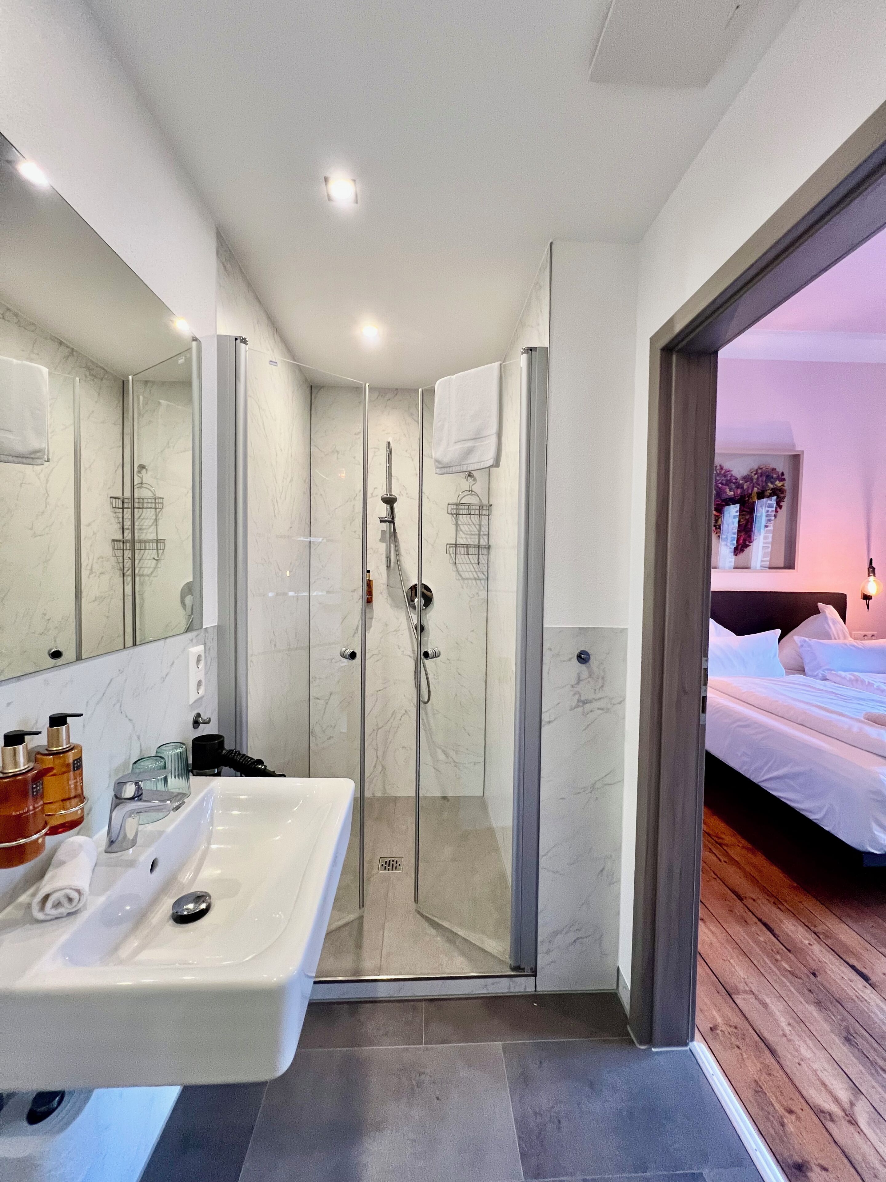 A modern bathroom with a glass-enclosed shower, a white sink with toiletries, and a large mirror.