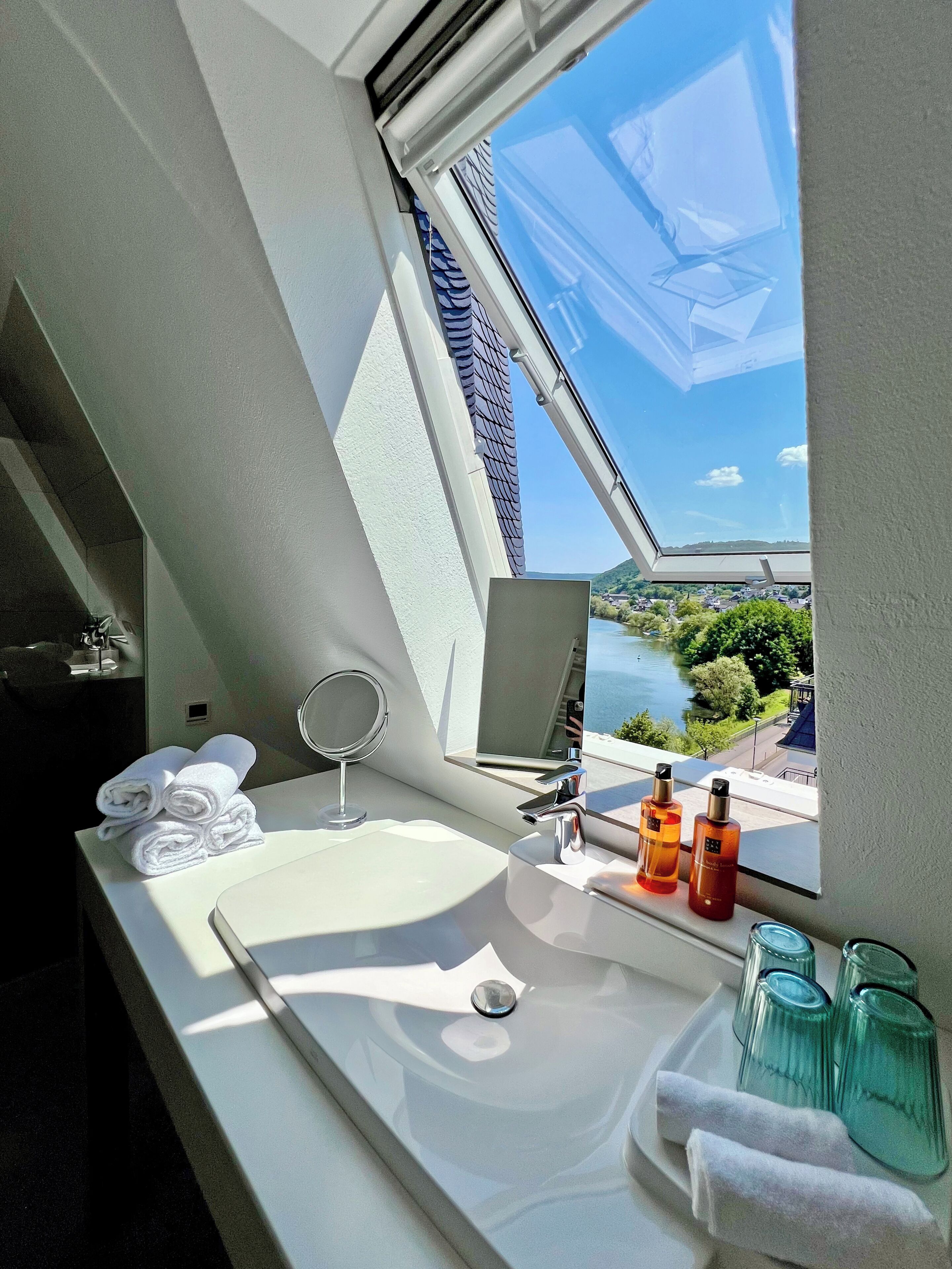 Une salle de bain avec un puits de lumière, un lavabo, un miroir et des articles de toilette.