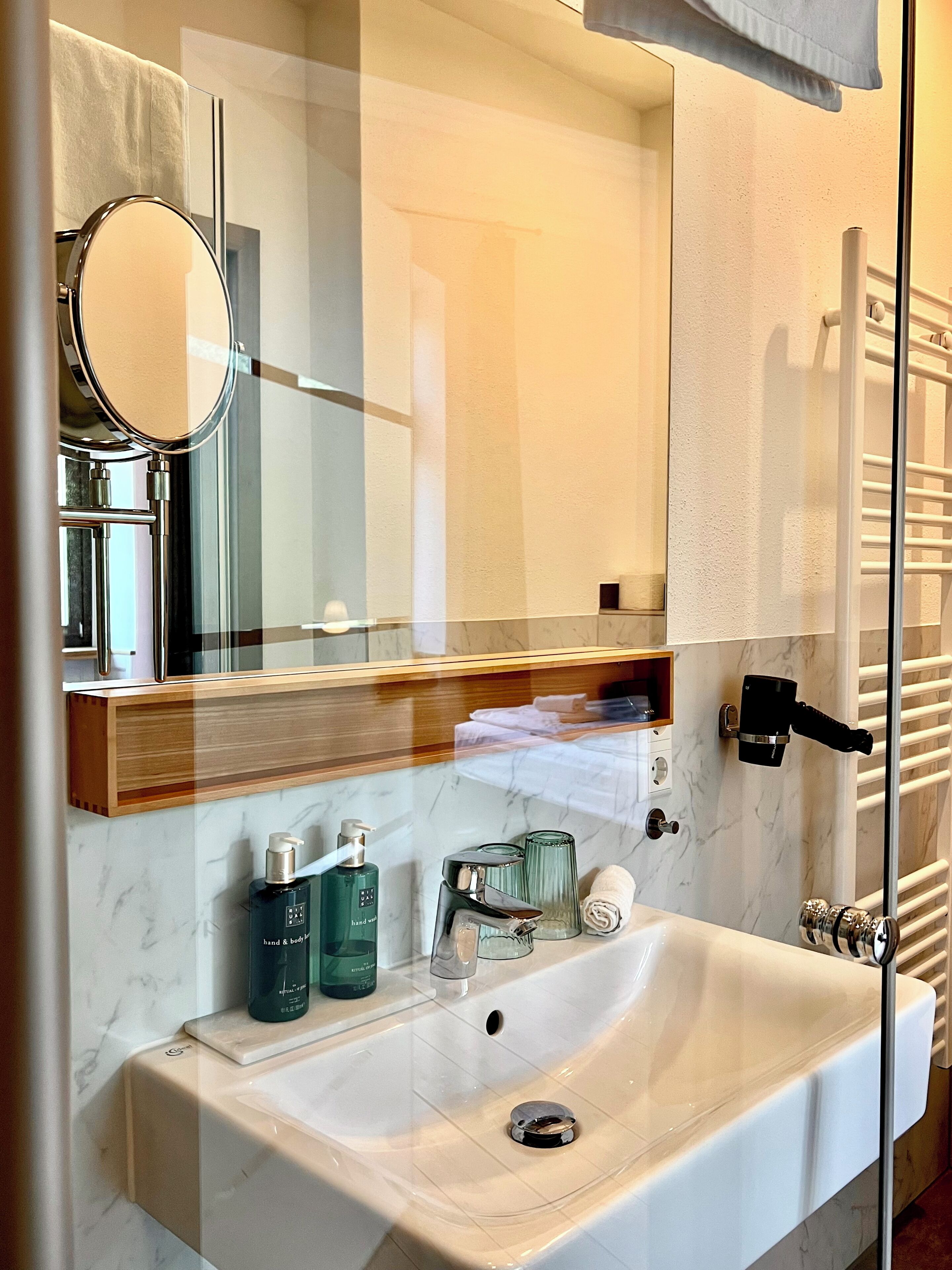A bathroom with a white sink, a mirror, a towel rack, and a glass shower enclosure.