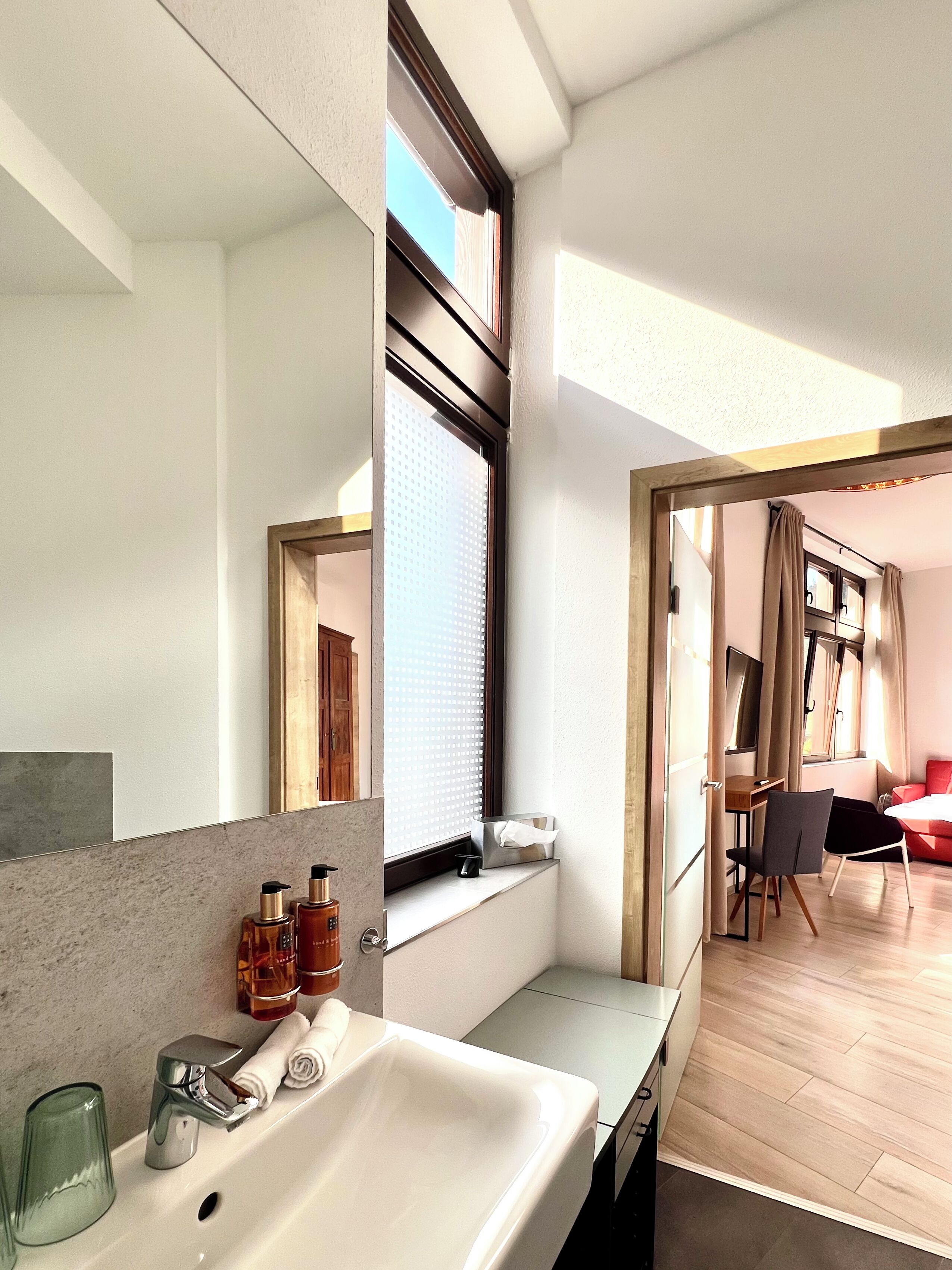 Un baño moderno con un espejo grande, un lavamanos y una ventana.