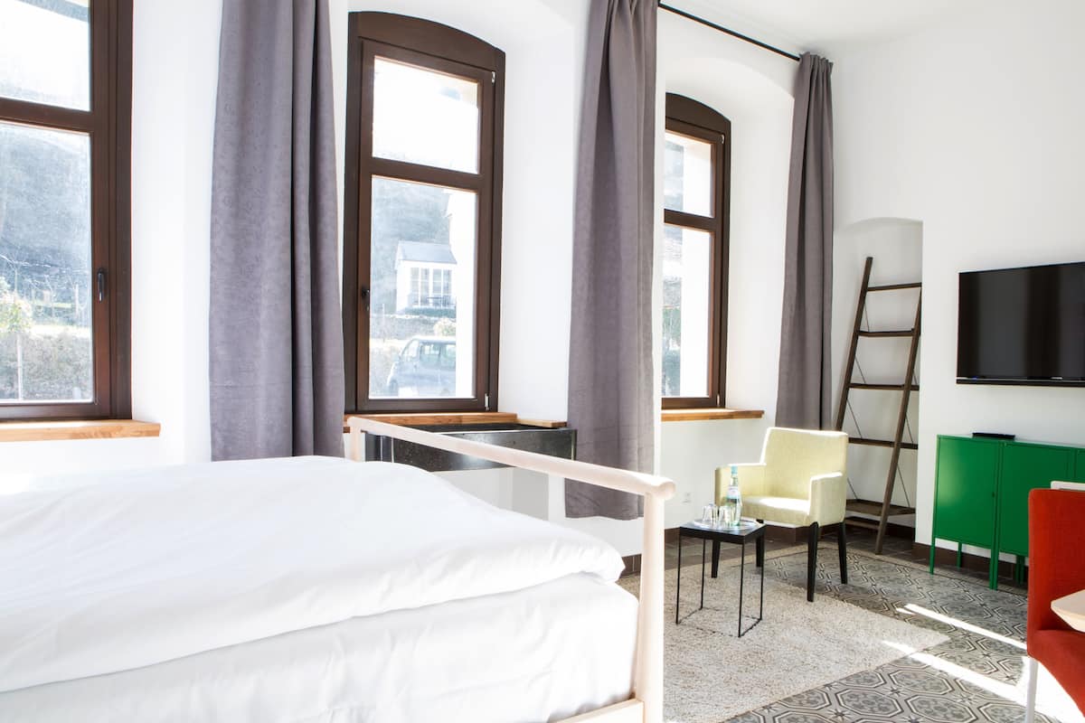 A hotel room with a bed, a chair, a TV, and a view of the outside.