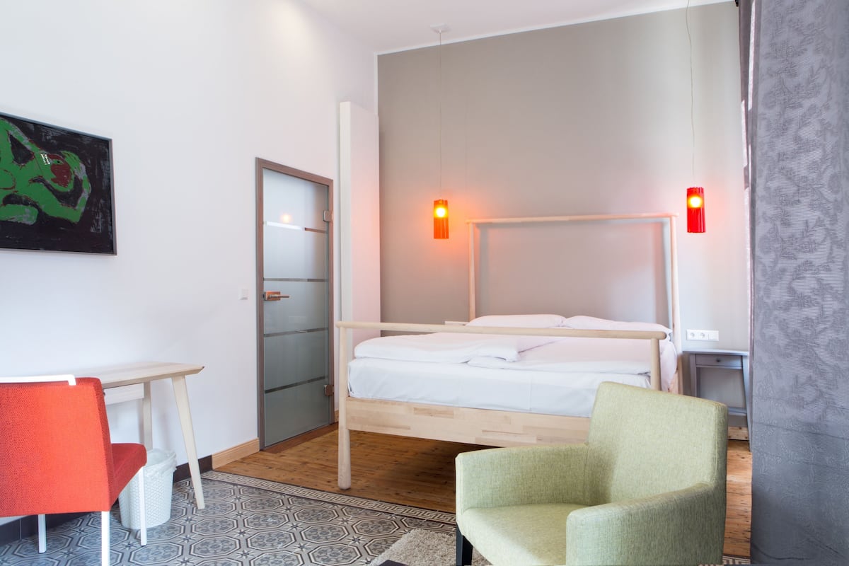 A room with a bed, a desk, a chair, and a painting on the wall.