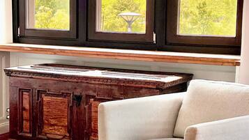 A room with a view of a green landscape through large windows, a wooden cabinet, and a white armchair.