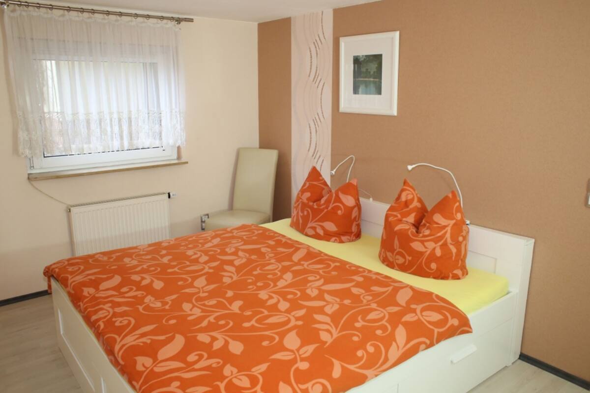 Une chambre à coucher avec un lit, une chaise, une fenêtre avec des rideaux et un tableau au mur.