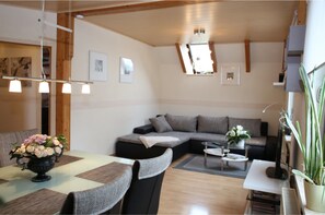 A modern living room with a sectional sofa, a dining table with chairs, a coffee table, and a potted plant.