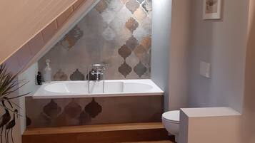 A bathroom with a bathtub, a toilet, and a patterned wall.