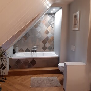 A bathroom with a bathtub, a toilet, and a patterned wall.