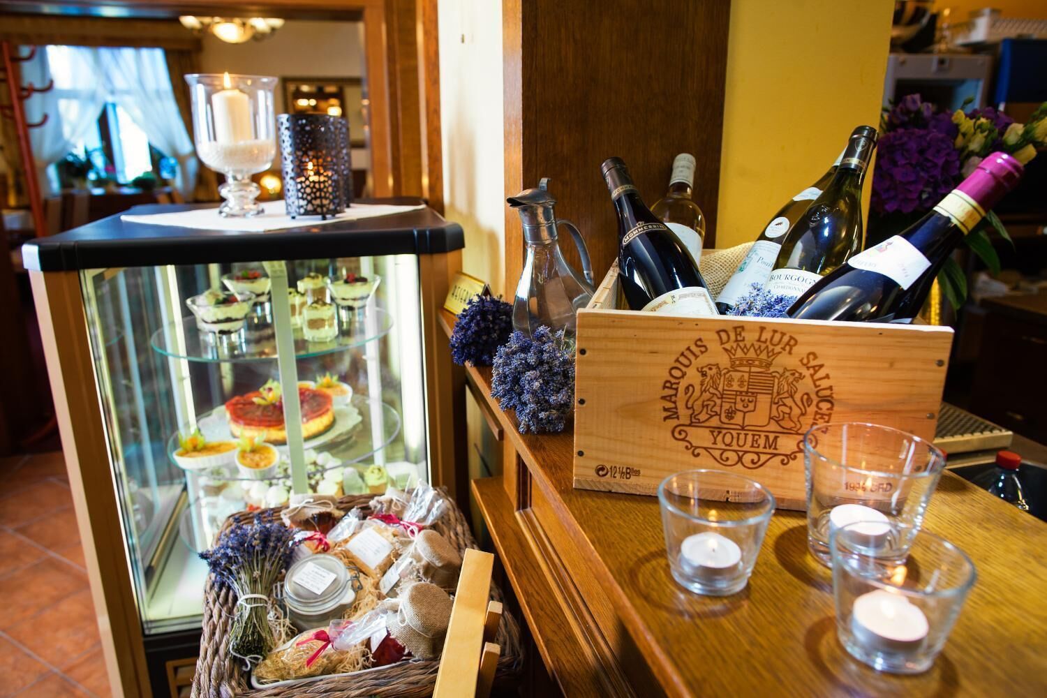 A bar area with a glass display case of desserts, a wooden box with wine bottles, and a candle holder.