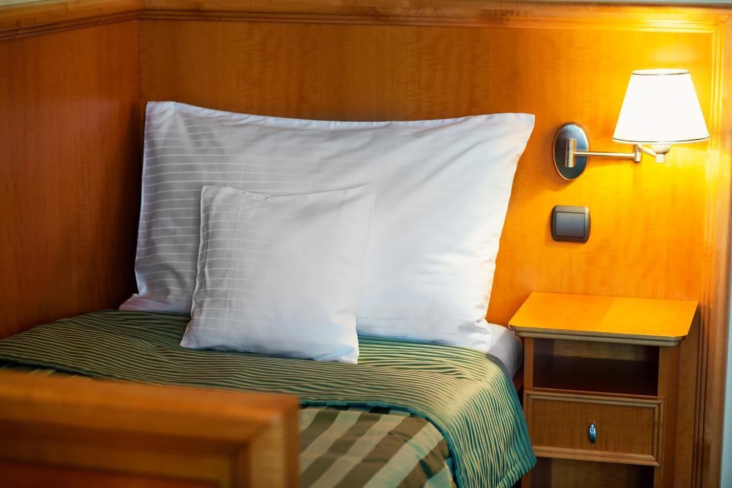 A neatly made bed with a striped bedspread, a wooden headboard, a bedside table with a lamp, and a small drawer.