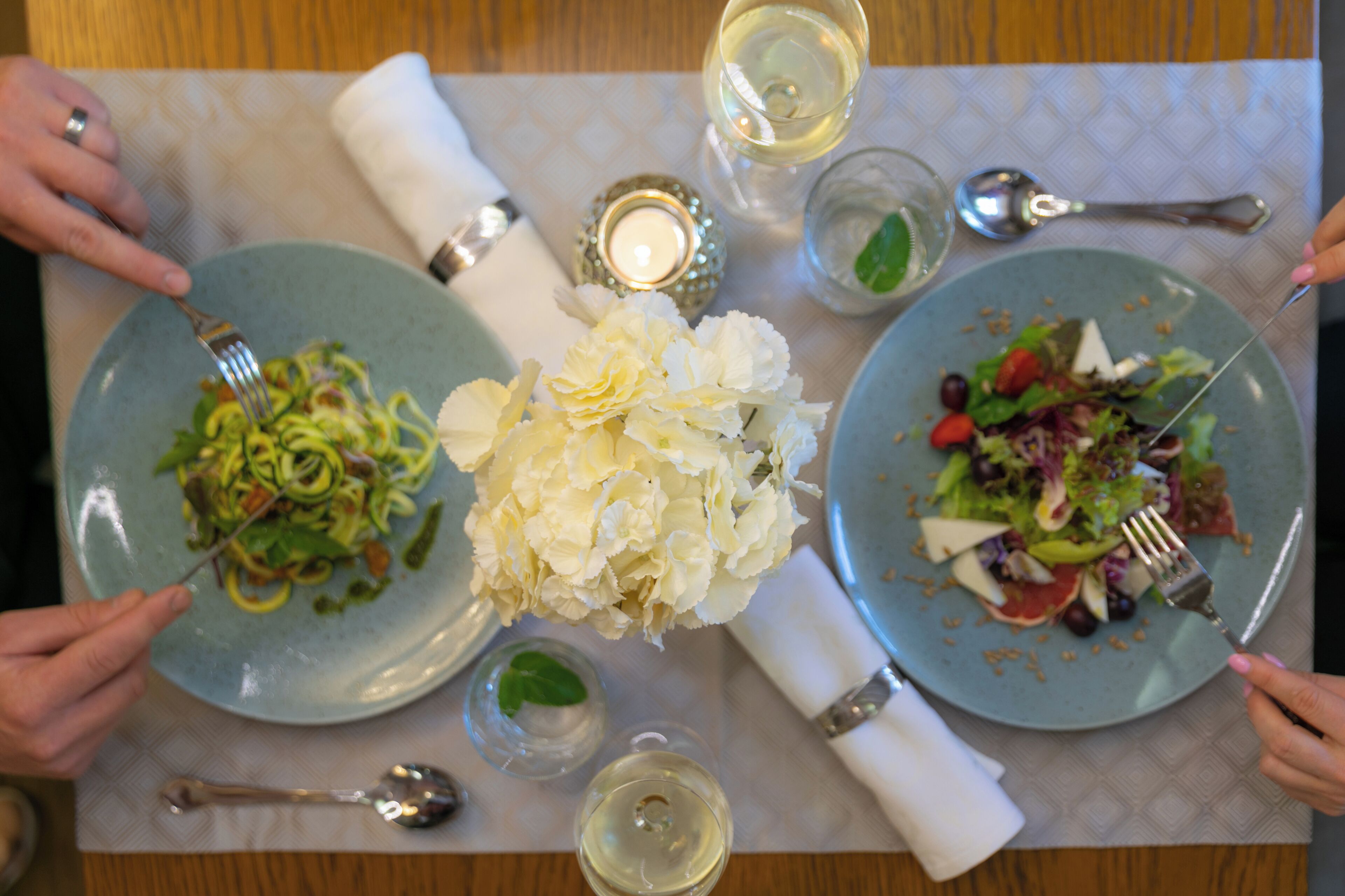 A table with two plates of food, a candle, and a vase of flowers.