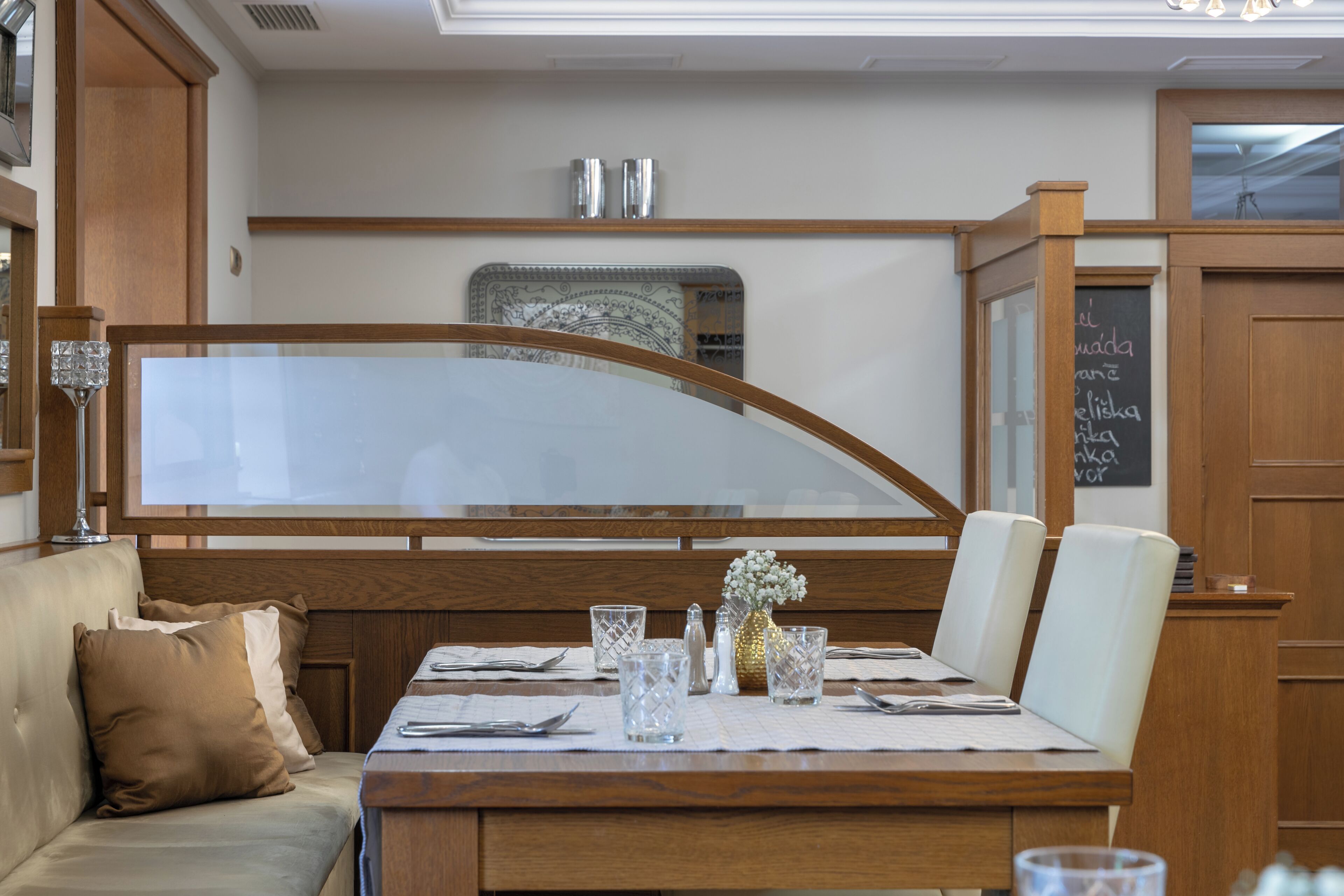 A dining area with a wooden table set for two, a cushioned bench, and a decorative vase.
