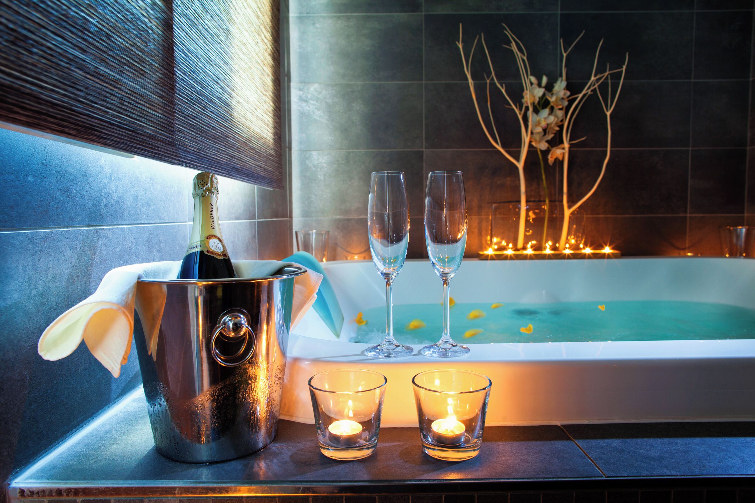 A bathtub with candles, a champagne bottle, and two glasses.