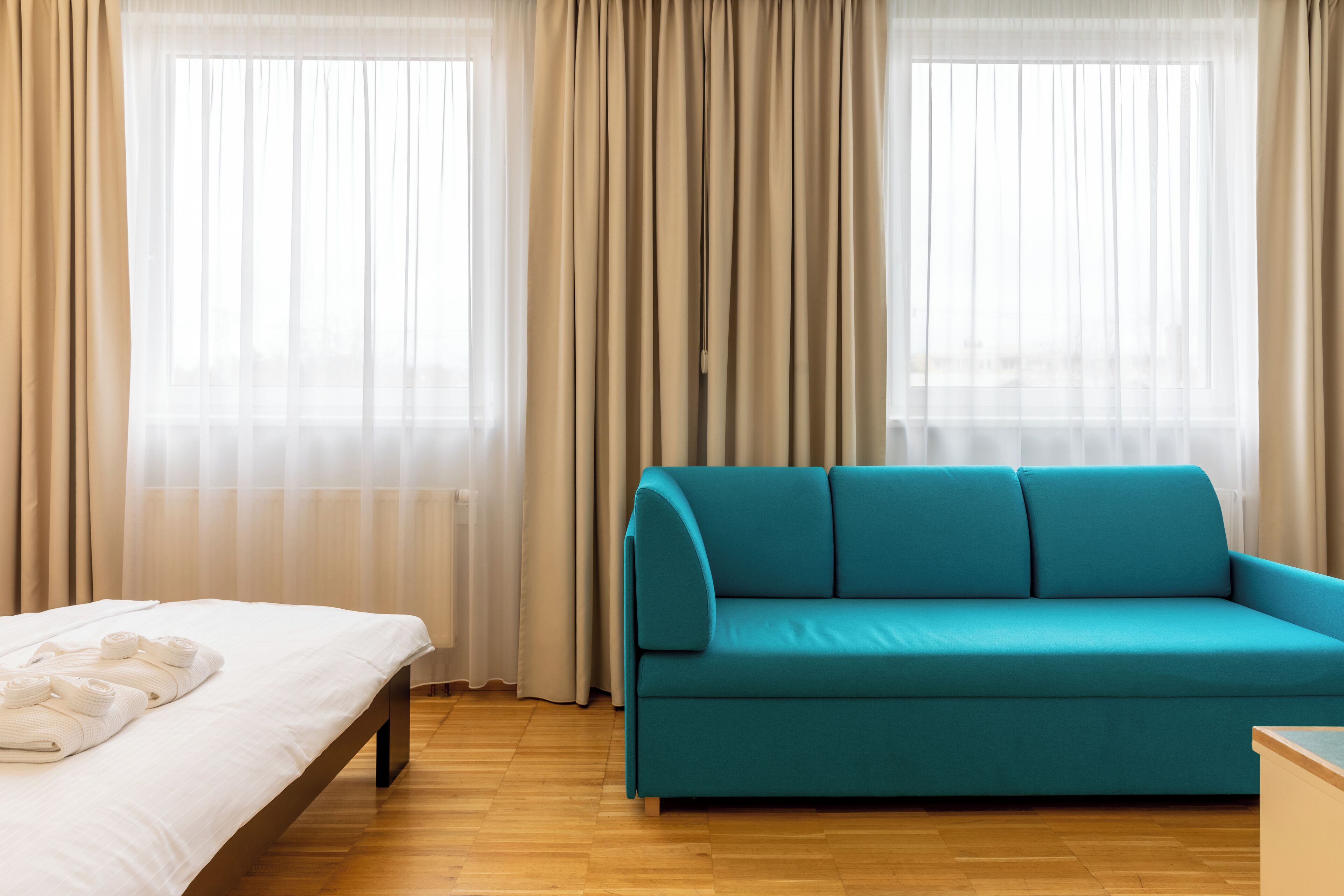 Una habitación con cama, un sofá verde azulado y una ventana con cortinas traslúcidas.