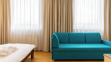 Una habitación con cama, un sofá verde azulado y una ventana con cortinas traslúcidas.