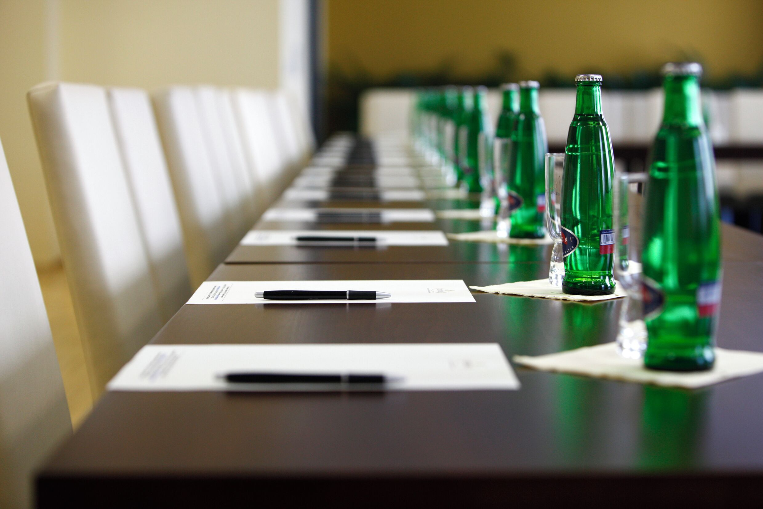 Ein Konferenztisch mit Dokumenten und Stiften, umgeben von grünen Flaschen.