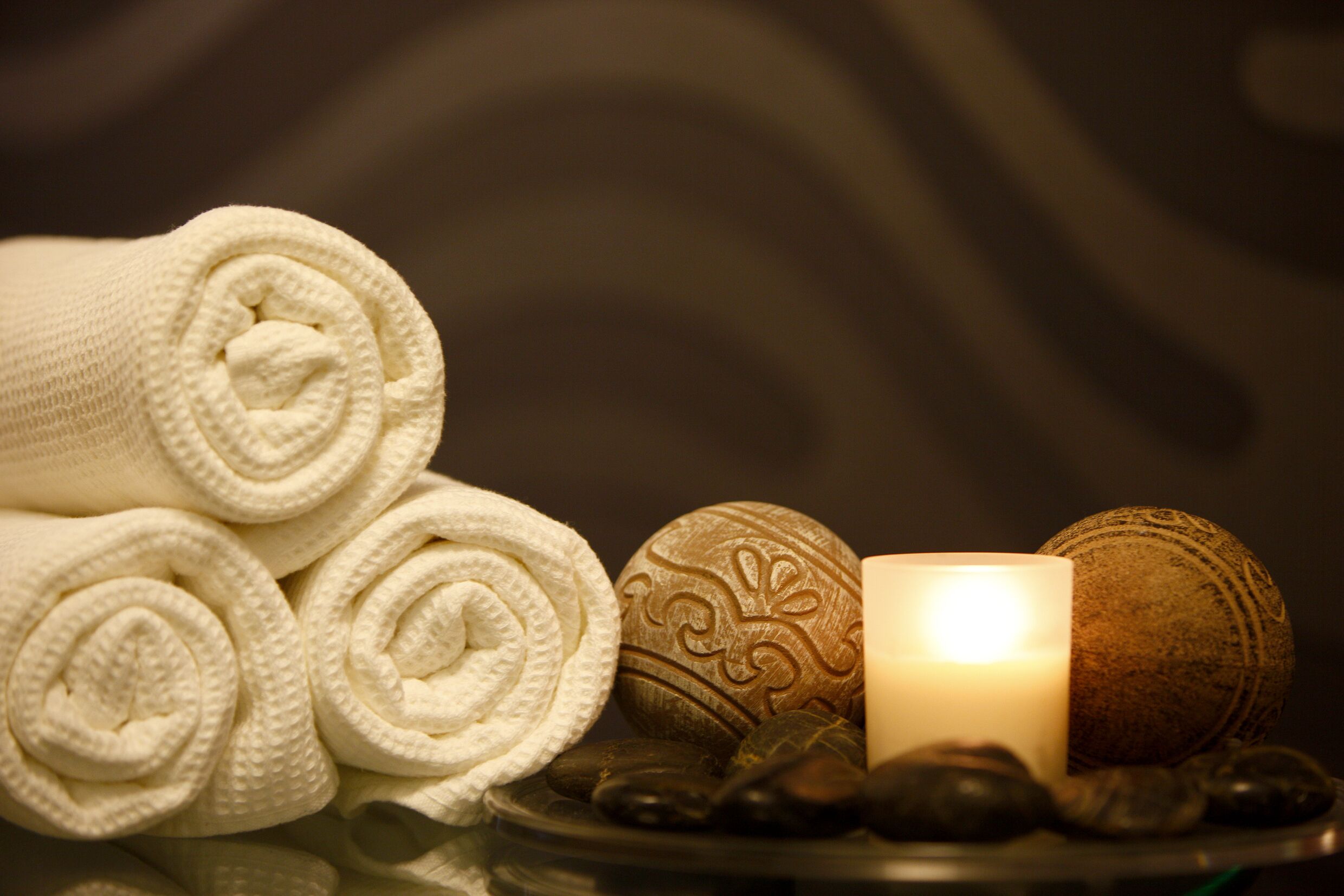 A spa setting with rolled towels, a lit candle, and decorative stones.