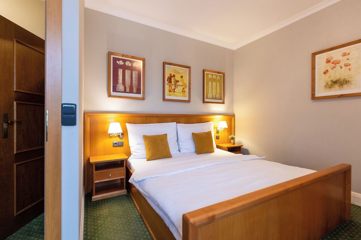 Una habitación de hotel con una cama de madera, dos mesitas de noche con lámparas y tres cuadros en la pared.