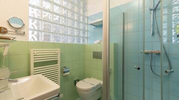 A bathroom with a glass shower enclosure, a white sink, and a toilet.