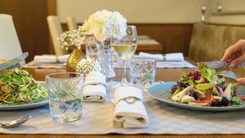 A dining table with two plates of food, a glass of white wine, and a vase with white flowers.