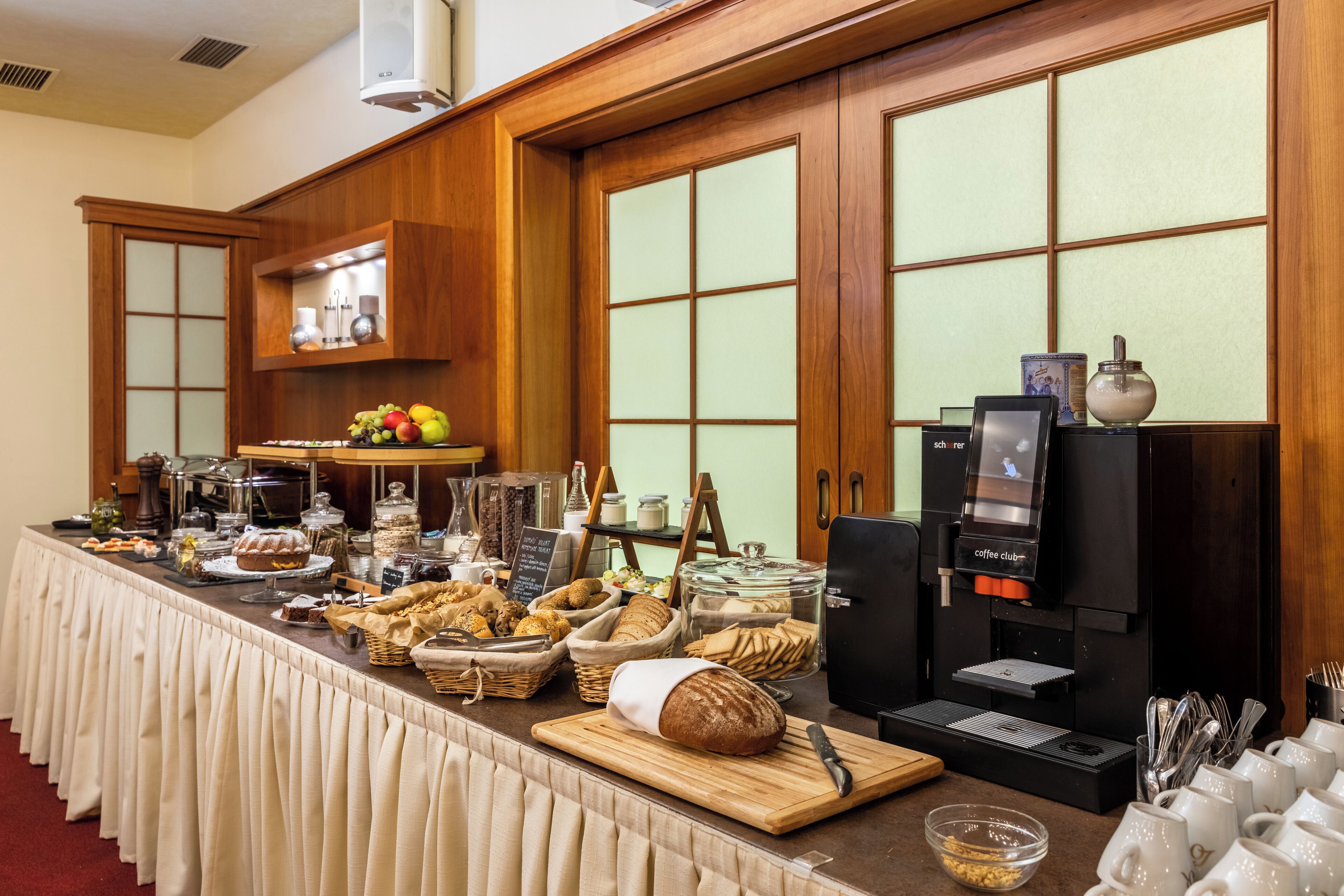 A buffet setup with various food items, a coffee machine, and a seating area with white mugs.