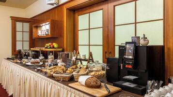 A buffet setup with various food items, a coffee machine, and a seating area with white mugs.