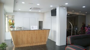 A reception area with a wooden counter, a black leather couch, and a fan. - Double Happiness Hotel (Seri Manjung)