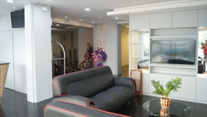 A modern living room with a grey sofa, a glass coffee table, and a flat-screen TV mounted on the wall. - Double Happiness Hotel (Seri Manjung)