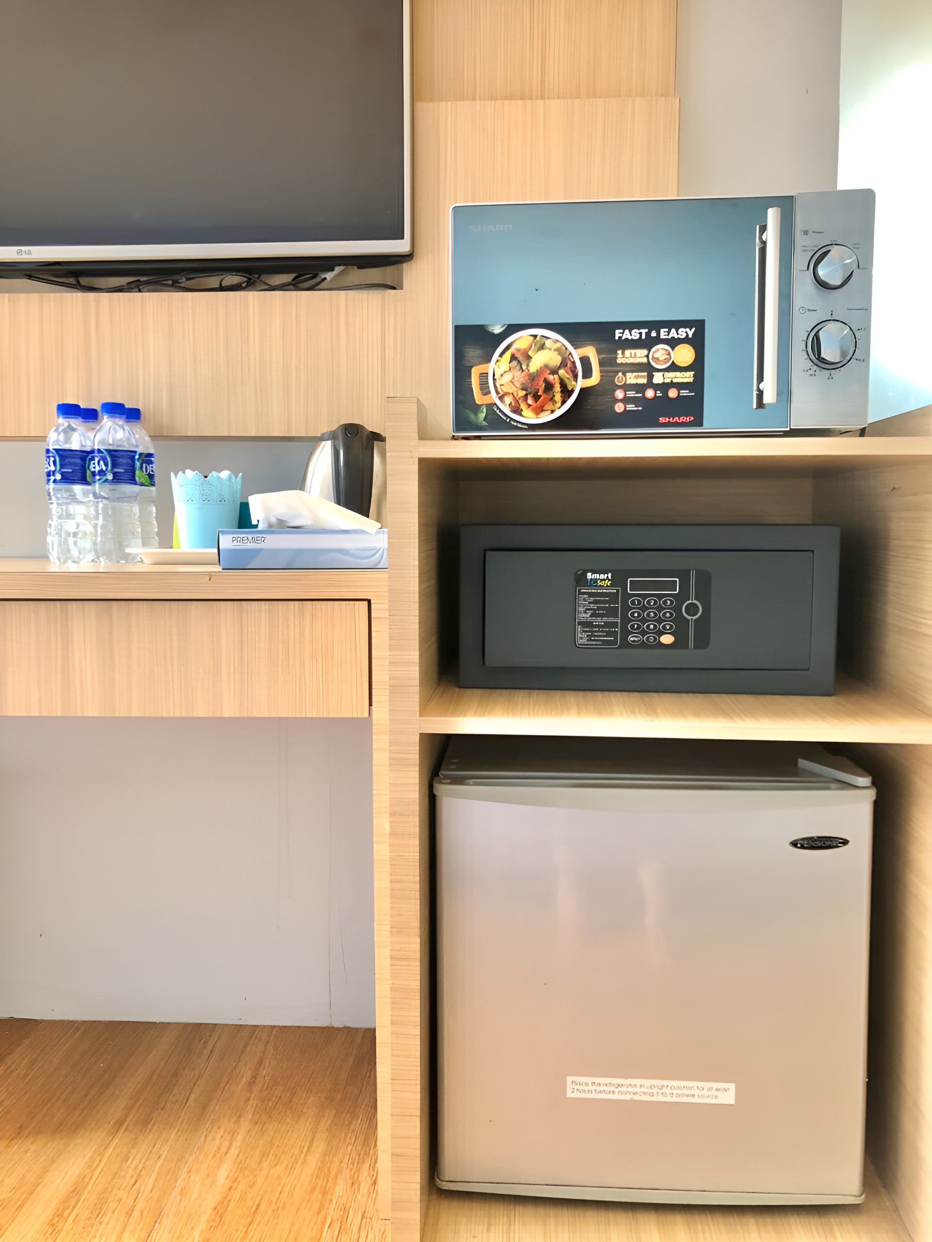 A kitchen area with a microwave, a refrigerator, and a television. There are water bottles and a tissue box on the counter.
