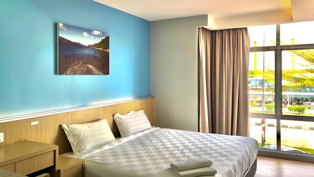 A hotel room with a large bed, a wooden nightstand, a desk, and a window with curtains. - Double Happiness Hotel (Seri Manjung)