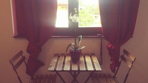A room with a wooden table and two chairs, a potted plant, and a window with curtains. - Ostello Le Tre Corone (Calendasco)