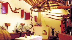 Una habitación rústica con vigas de madera, una mesa con mantel blanco y diversos objetos y herramientas de madera en las paredes.