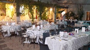 Un salón de banquetes con mesas dispuestas para un evento formal, rodeado de follaje y columnas arquitectónicas.