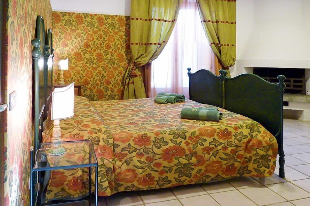 A bedroom with floral-patterned bedding, a wooden headboard, a bedside table with a lamp, and curtains.