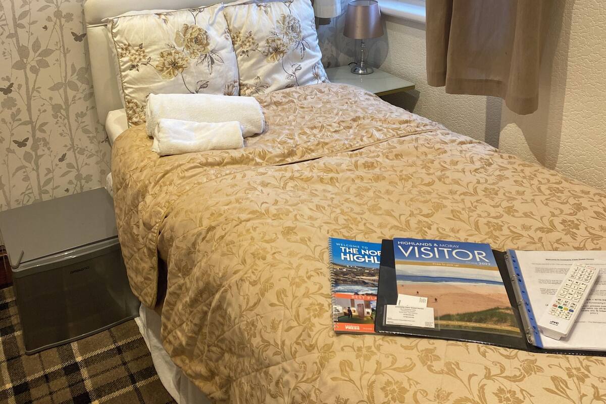 A neatly made bed with a floral duvet, a laptop on the floor, and a welcome booklet on the bed.