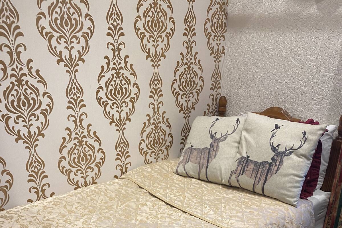 A neatly made bed with a floral patterned bedspread, a pillow with a deer design, and a checkered floor.