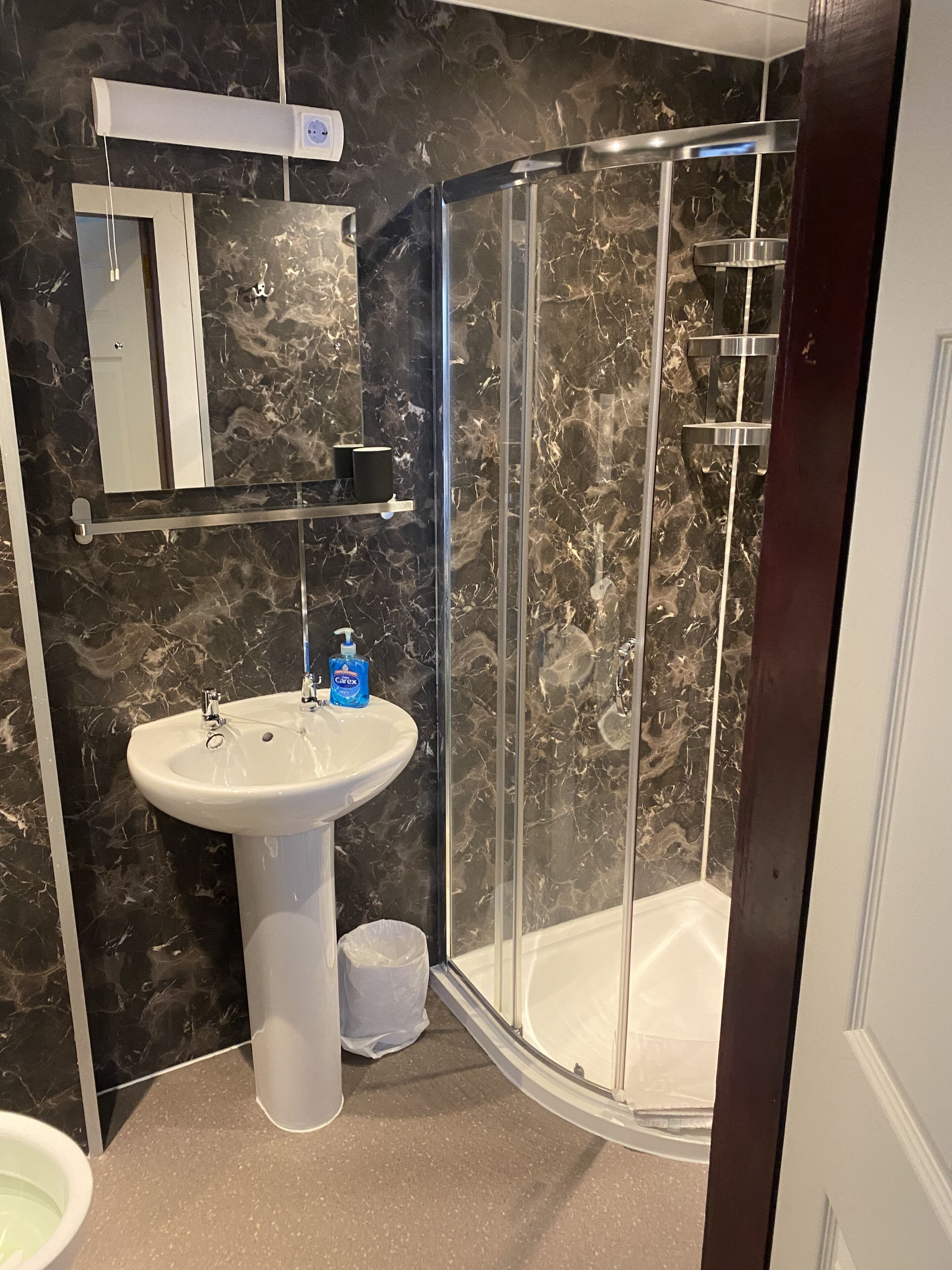 Un baño moderno con cabina de ducha de vidrio, lavamanos pedestal y salpicadero de mármol.