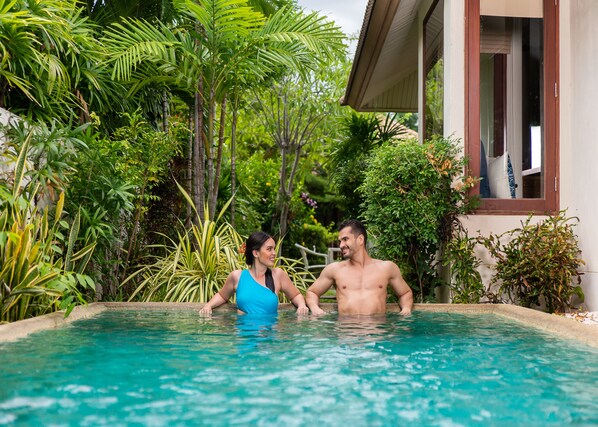 Une piscine entourée d’une végétation luxuriante et un bâtiment doté d’une fenêtre.