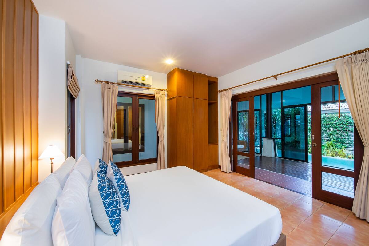 Ein Hotelzimmer mit einem großen Bett, einem Holzschrank und einer Glasschiebetür, die auf einen Balkon mit Blick auf Grünflächen führt.
