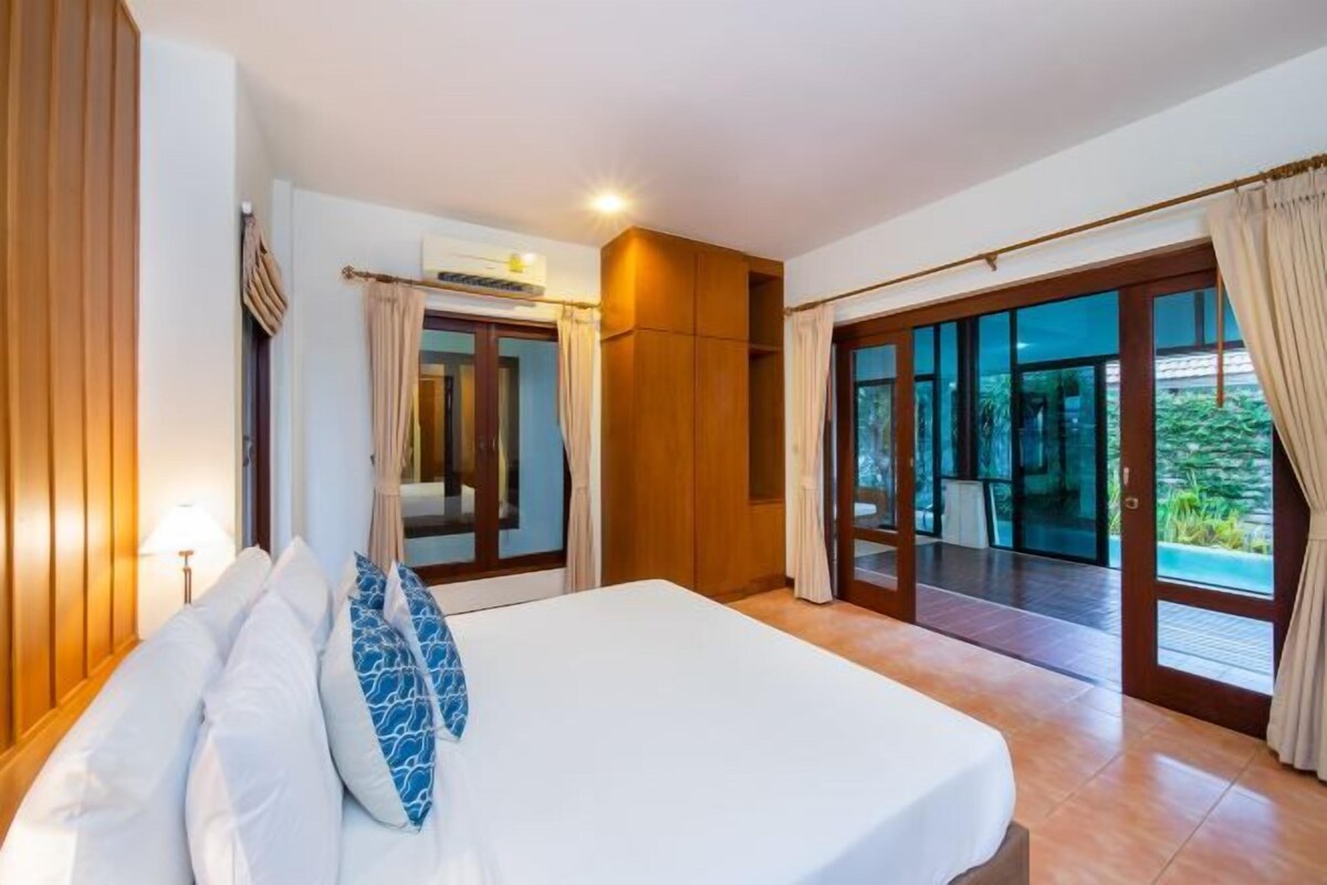 A hotel room with a large bed, a sliding glass door leading to a balcony, and a wooden wardrobe.