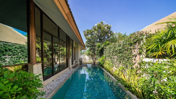 A swimming pool with tiled edges, surrounded by lush greenery and a building with large windows. - Blu Marine Hua Hin Resort and Villas (Hua Hin)