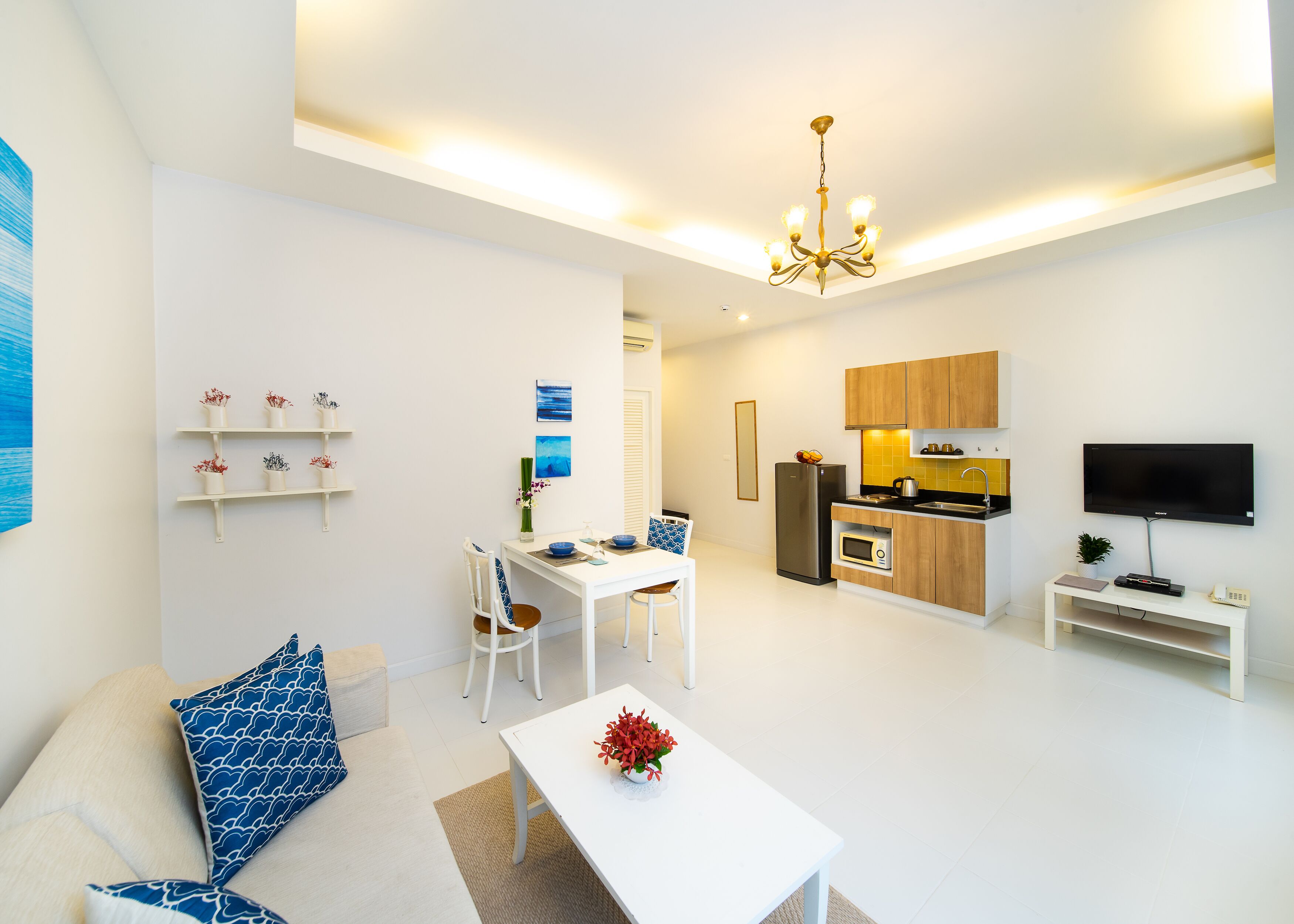 Un salon moderne avec un canapé blanc, une table à manger et un coin cuisine doté de meubles en bois et d’un téléviseur à écran plat.
