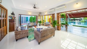 A spacious living area with wicker furniture, a ceiling fan, and a view of a pool and garden. - Blu Marine Hua Hin Resort and Villas (Hua Hin)