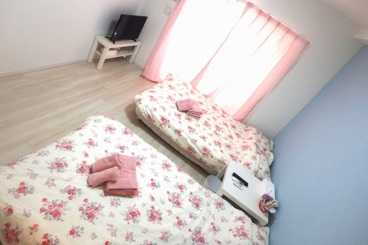 A bedroom with two beds, a TV on a small table, and a window with curtains.
