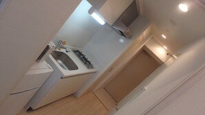 A narrow hallway with a kitchen area featuring a sink, stove, and cabinets. - YADO at Shinsaibashi Namba ExMin (Osaka)