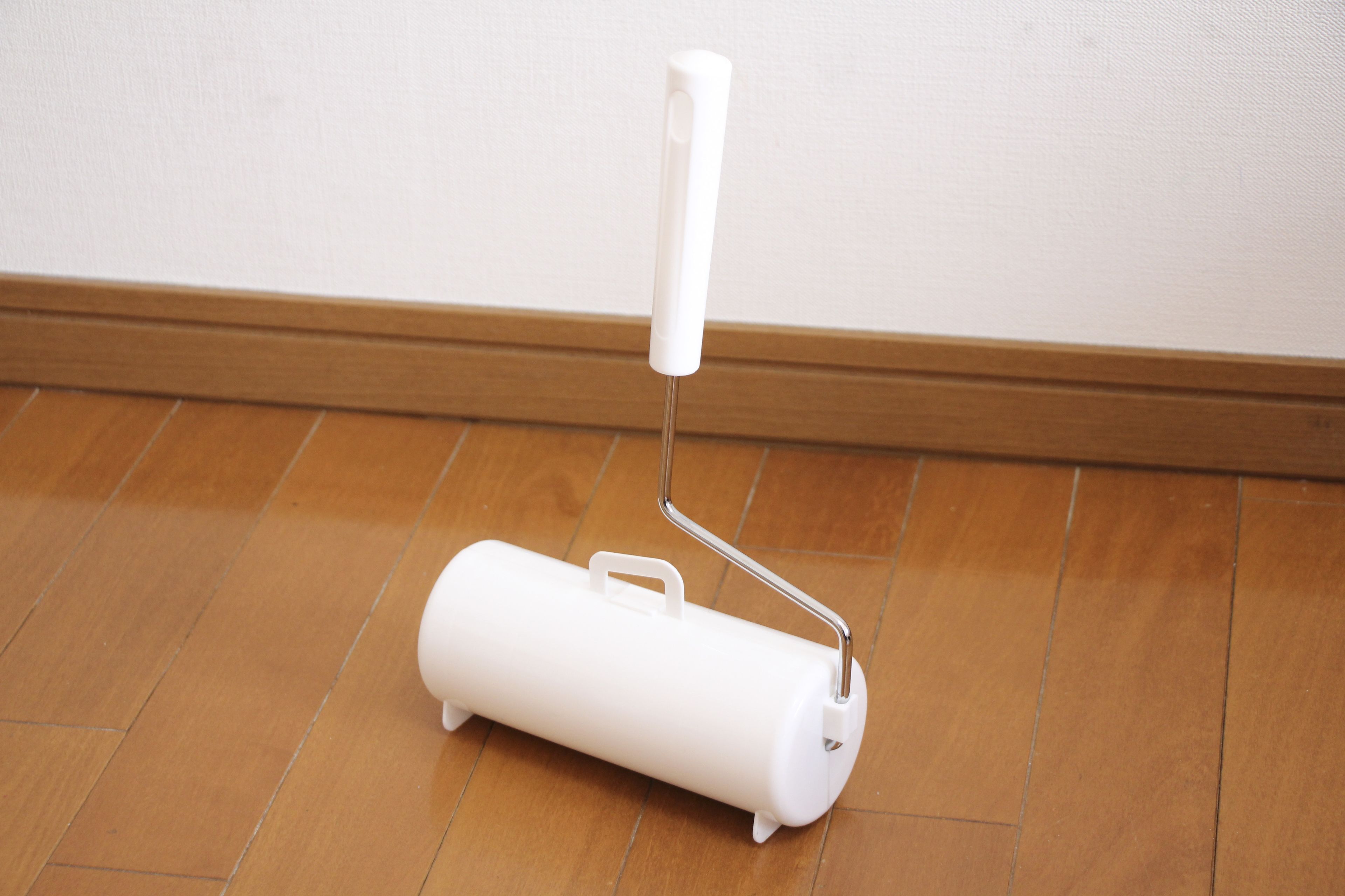 A white paint roller on a wooden floor.