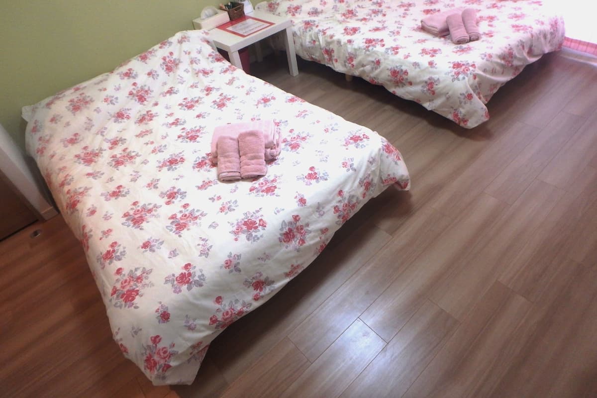 Two single beds with floral bedding, a bedside table with a lamp, and a window with curtains.
