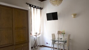 Et værelse med en stor træskab, et glas spisebord med stole, et fladskærms-TV monteret på væggen og en lysekrone.